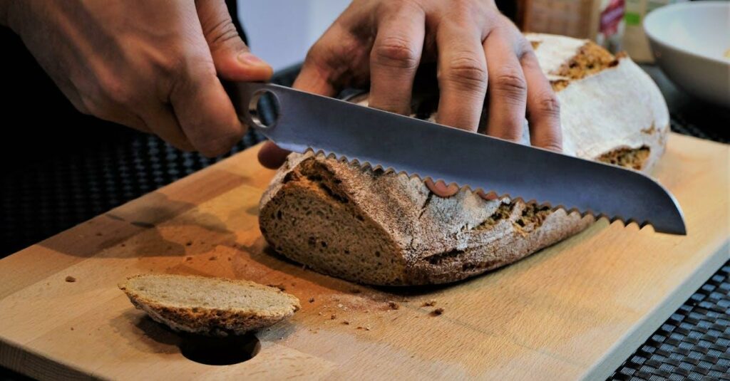 Person slicing artisan bread on a wooden cutting board with a serrated knife.